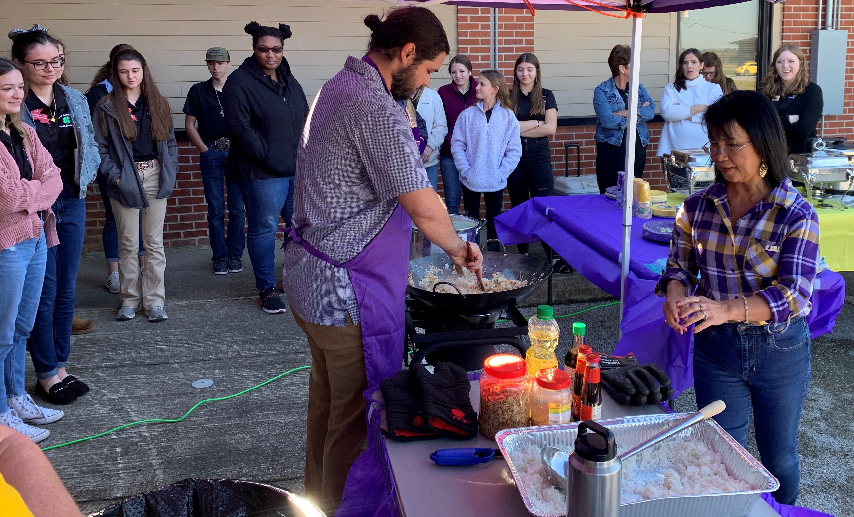 Students observe a rice cooking demonstration by two people.